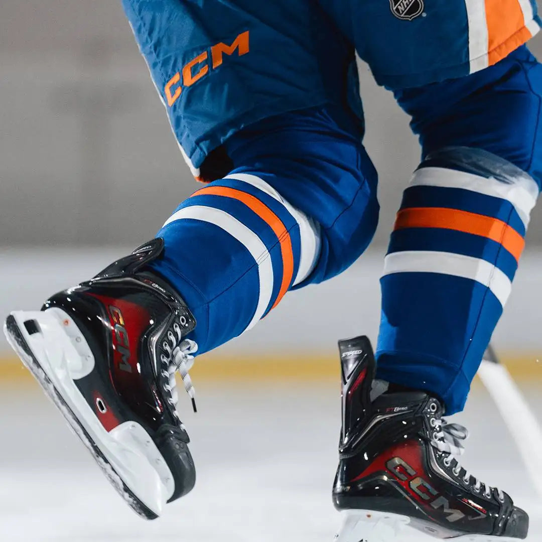 Black and red ccm hockey skates with white laces, worn by an athlete in blue gear.