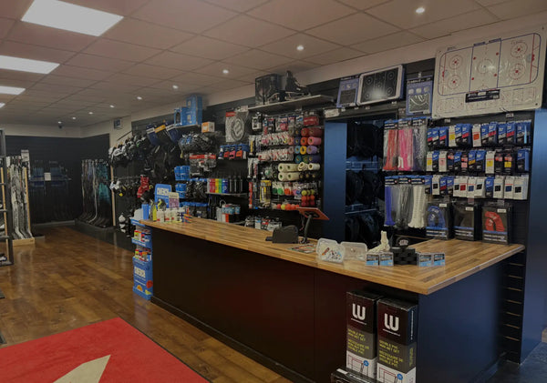 Dark wood counter with a light brown wooden top and black sides, featuring various sports equipment items displayed on shelves behind it.