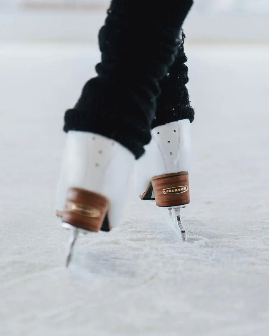White figure skates with brown leather ankle guards and silver blades, featuring a ’fackel’ logo on the guard.